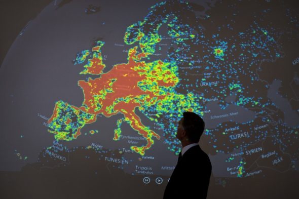A person standing in front of a large heatmap projection of Europe,displaying various data points.