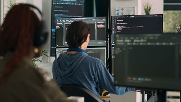 A person sitting at a desk in front of multiple computer monitors displaying code